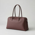 Brown leather handbag on a wooden surface with a laptop and glasses nearby.